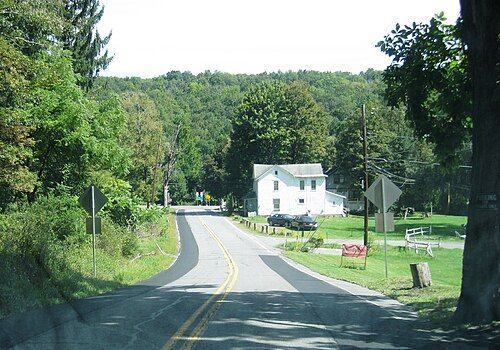 Effort ,PA A paved road leads toward a white house surrounded by green trees and a grassy lawn under a clear sky.