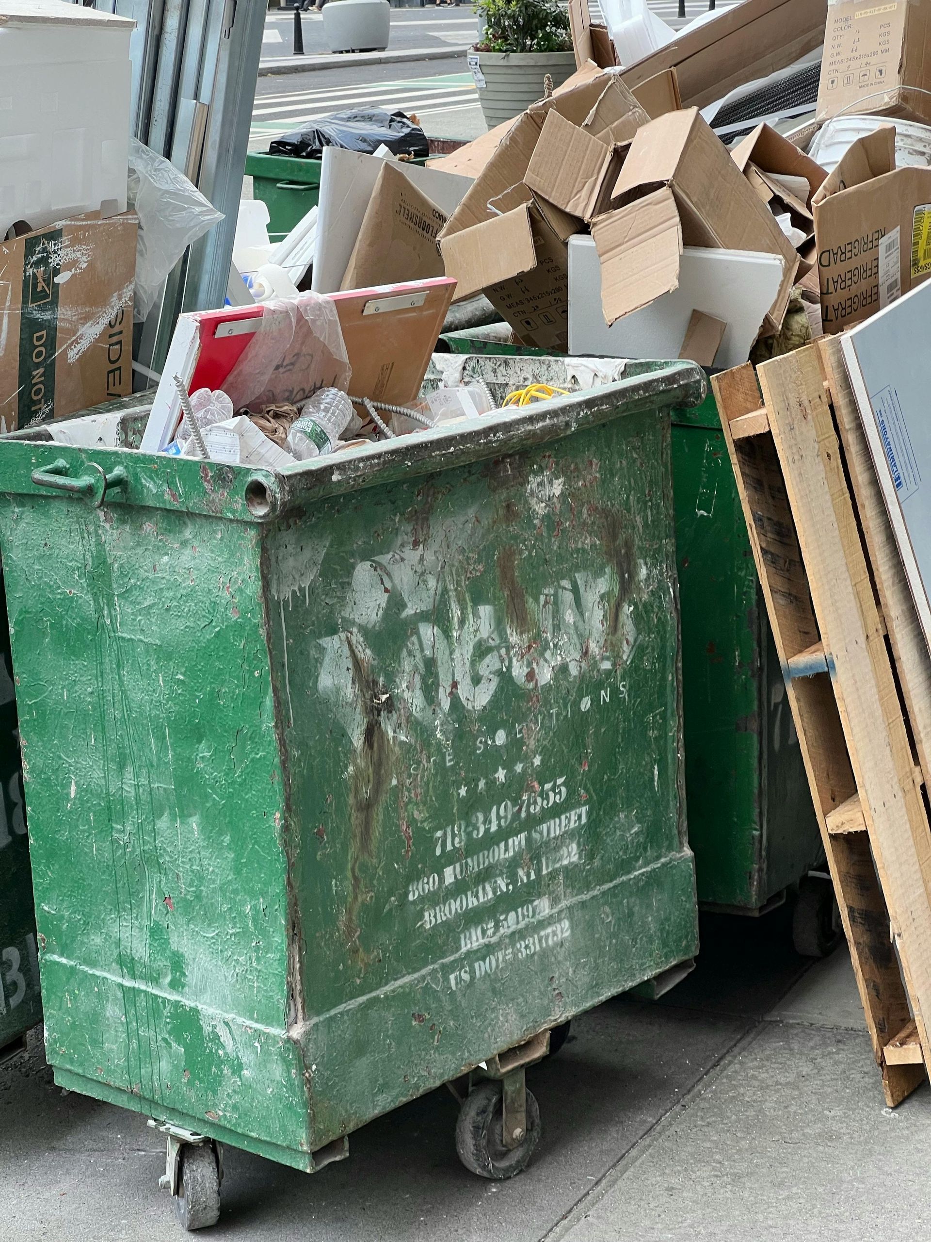 A green dumpster filled with cardboard boxes and pallets.