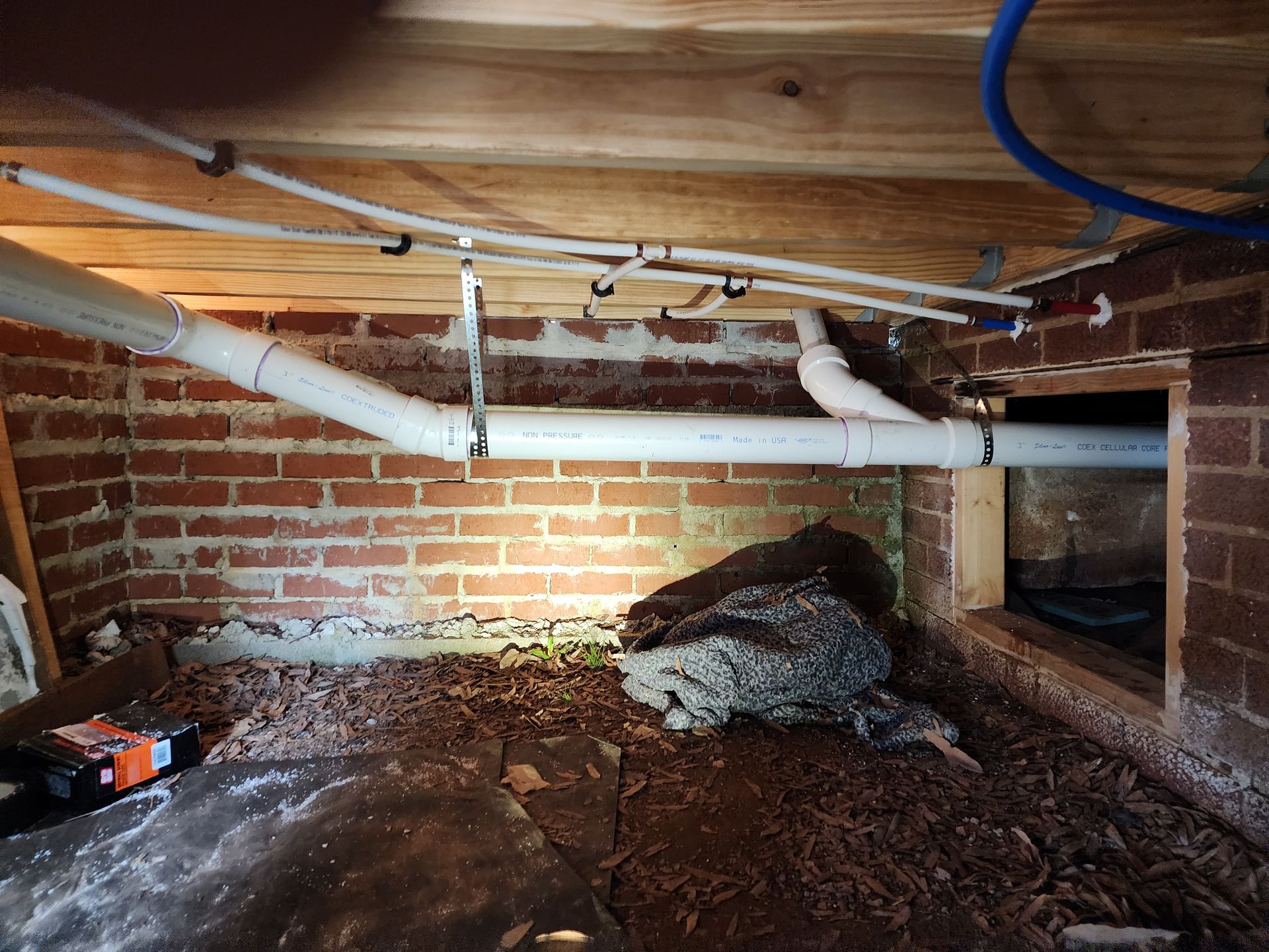 View of crawlspace with pipes and brick foundation. Debris covers the ground.