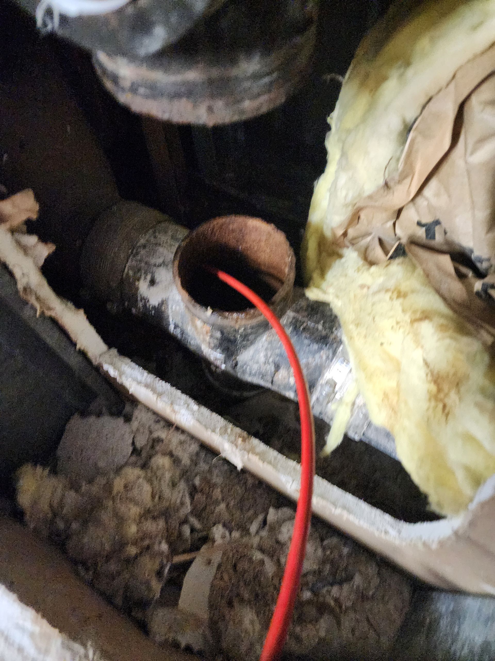 Red wire protruding from a rusty pipe in a cluttered, dark area.