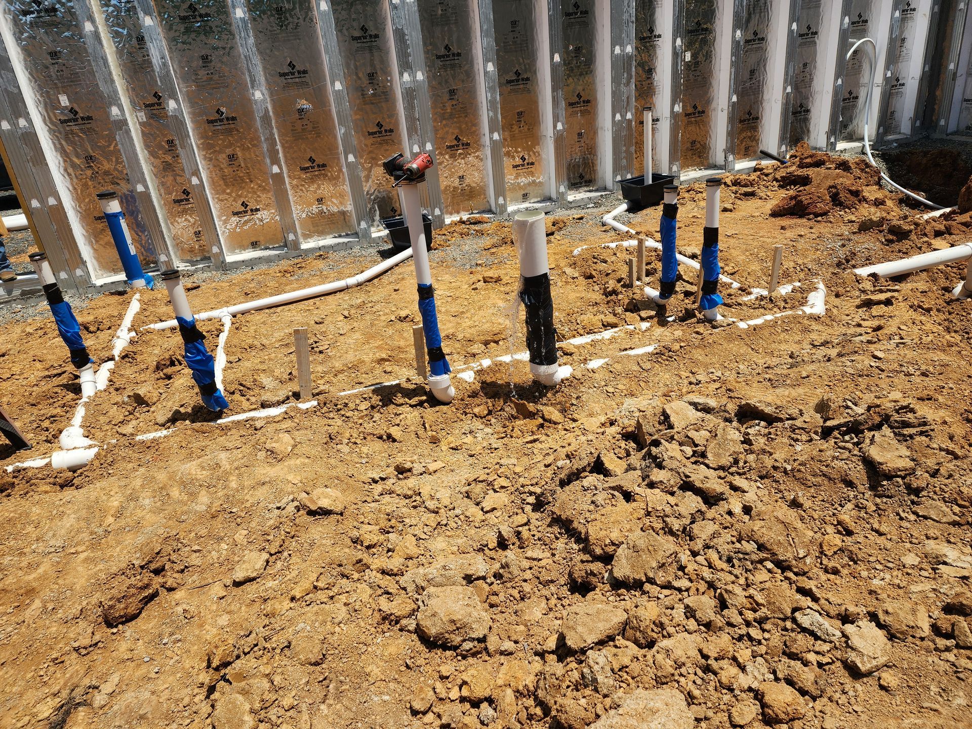Pipes installed in dirt next to a wall under construction. Blue and white pipes are visible.
