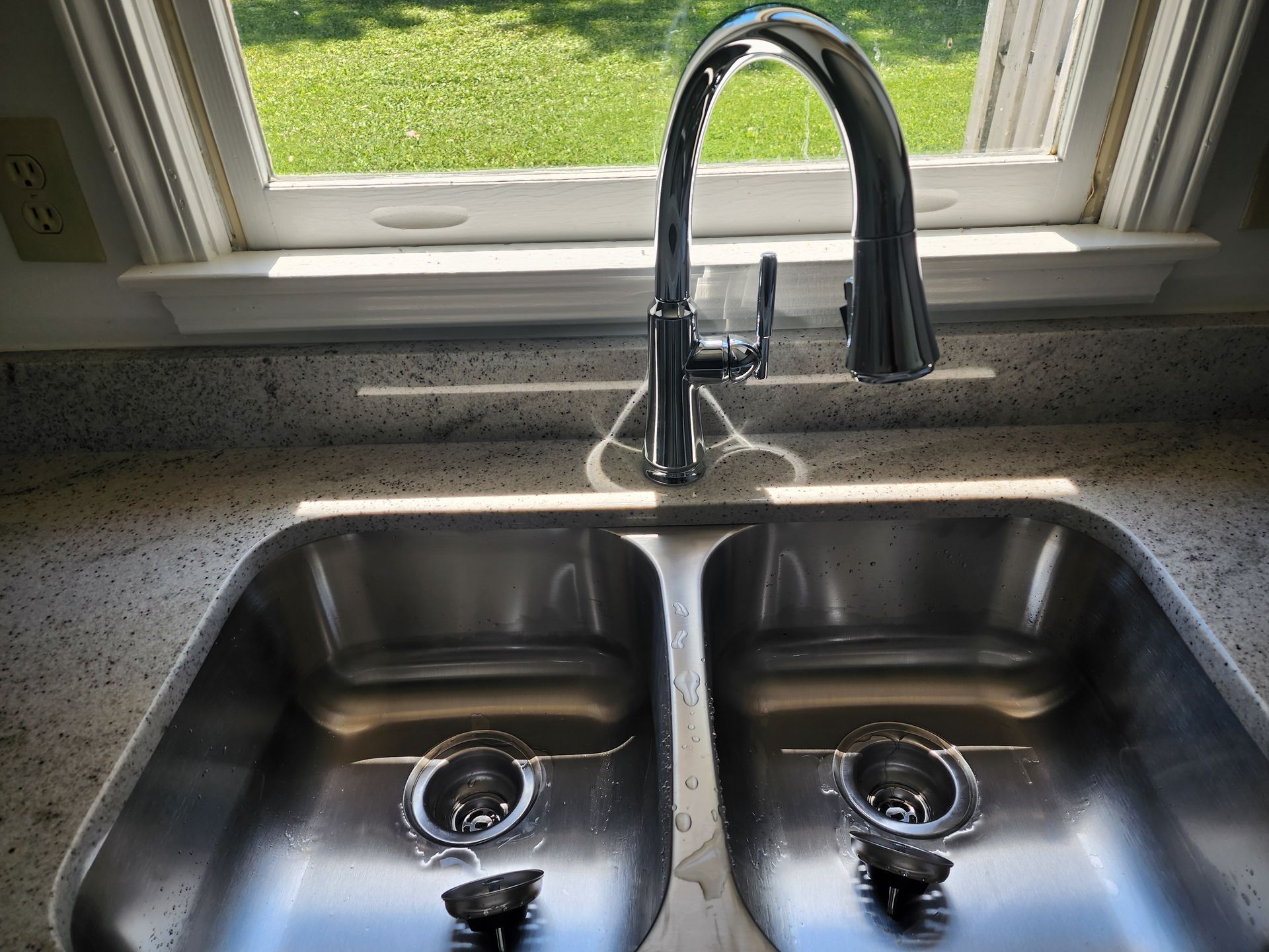 Stainless steel double sink with faucet, granite countertop, and window in background.