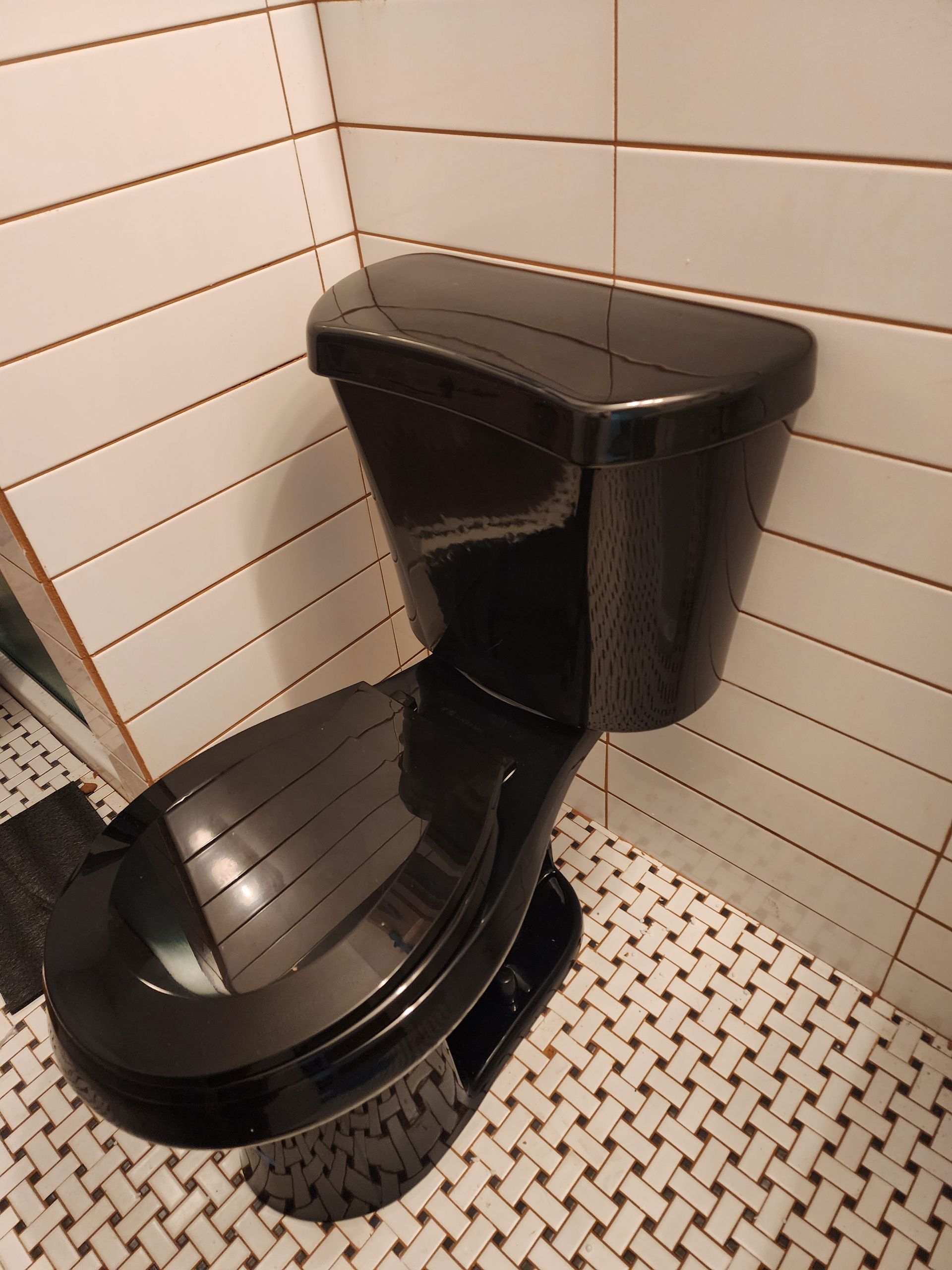 Black toilet in a bathroom with white tile walls and a patterned tile floor.