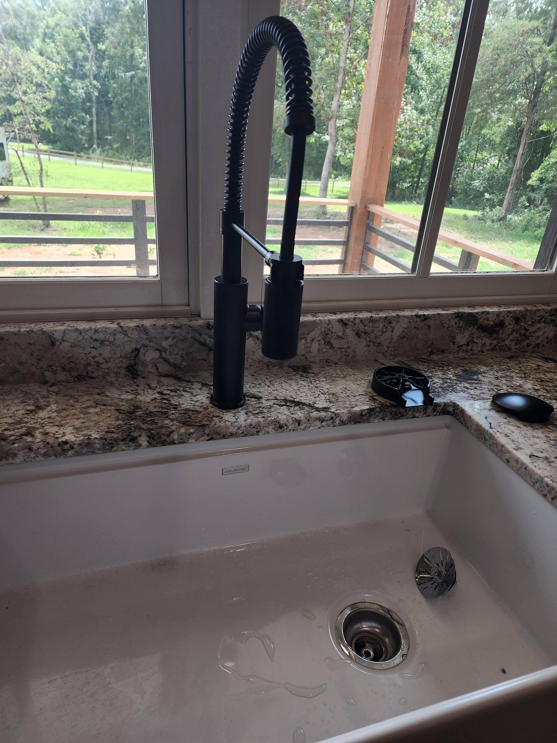 Black kitchen faucet over white sink, set in a granite countertop in front of a window.