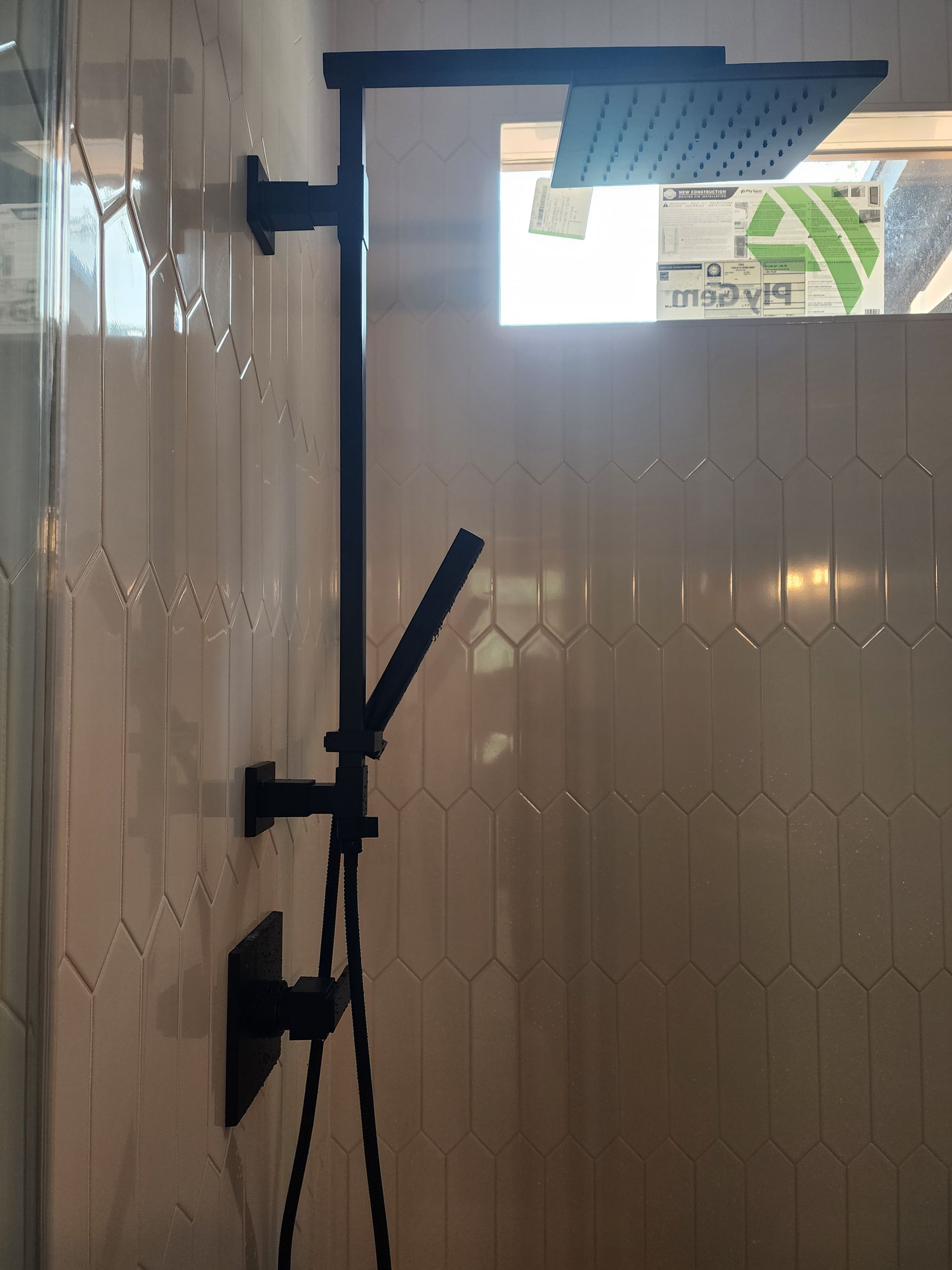 Black shower fixture on white tiled wall with a window.