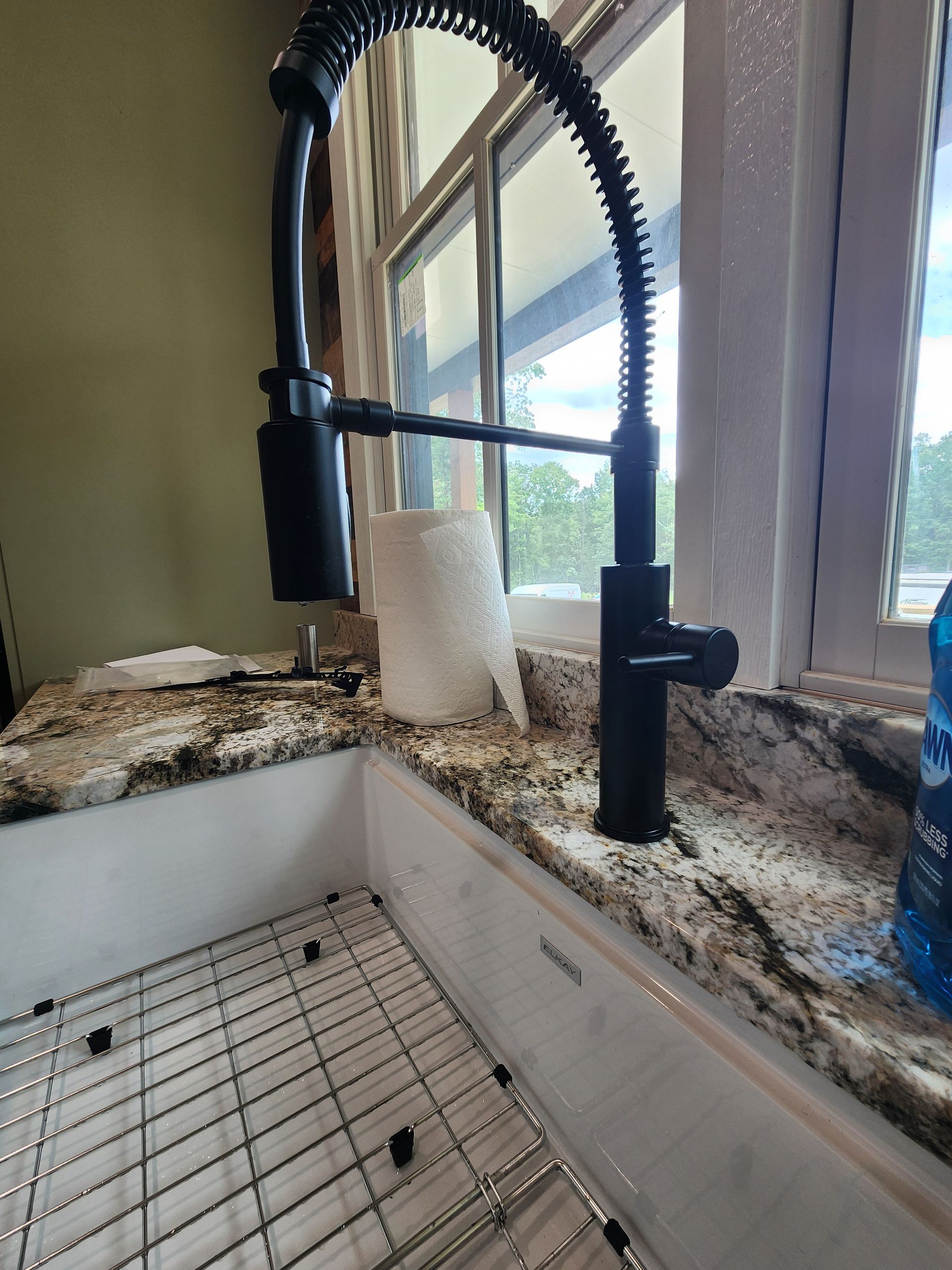 Black kitchen faucet with a coil, installed on a granite countertop, next to a window.