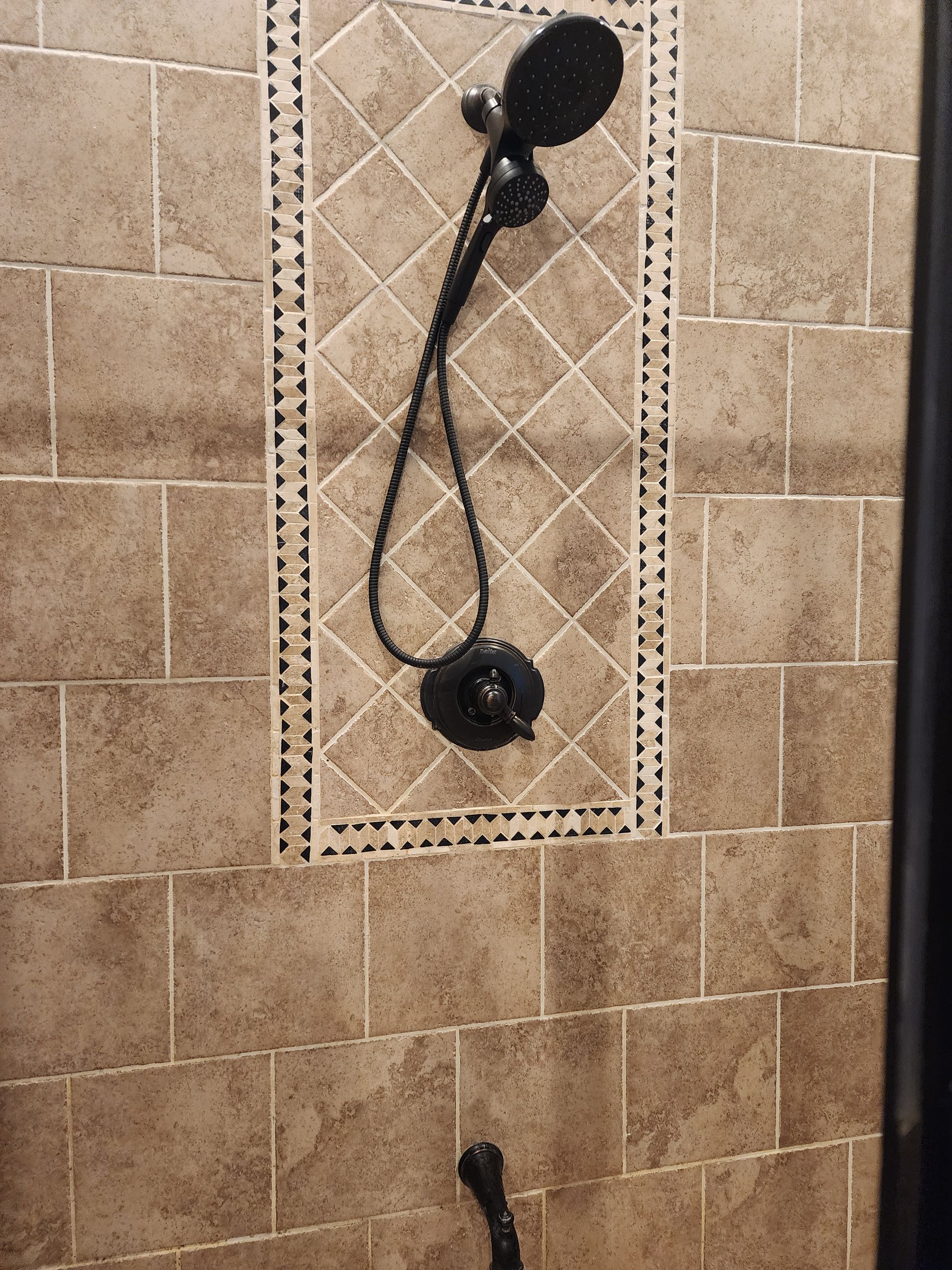 Shower with dark fixtures against tan tiled walls.