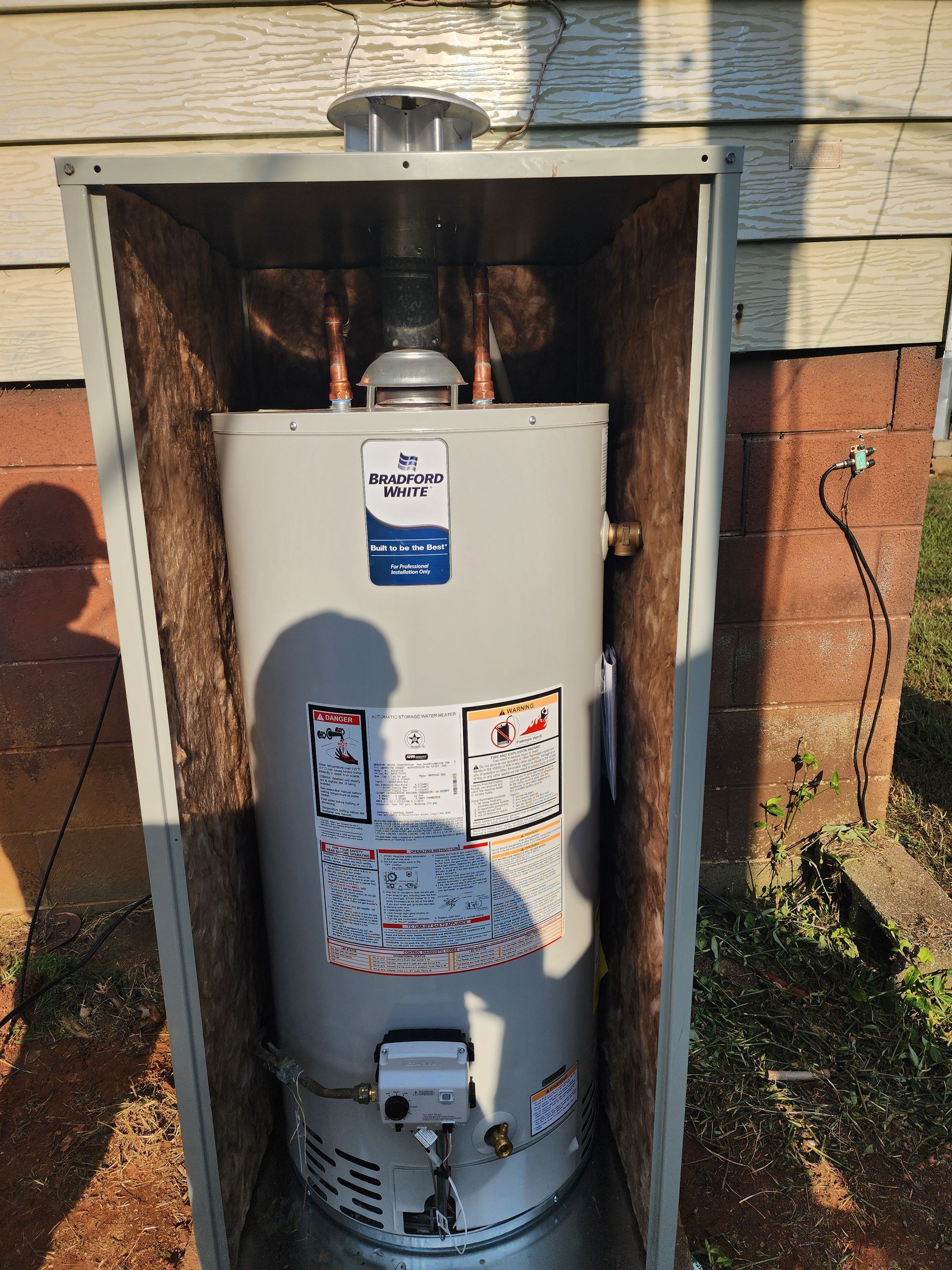 Water heater inside an insulated metal enclosure outdoors.
