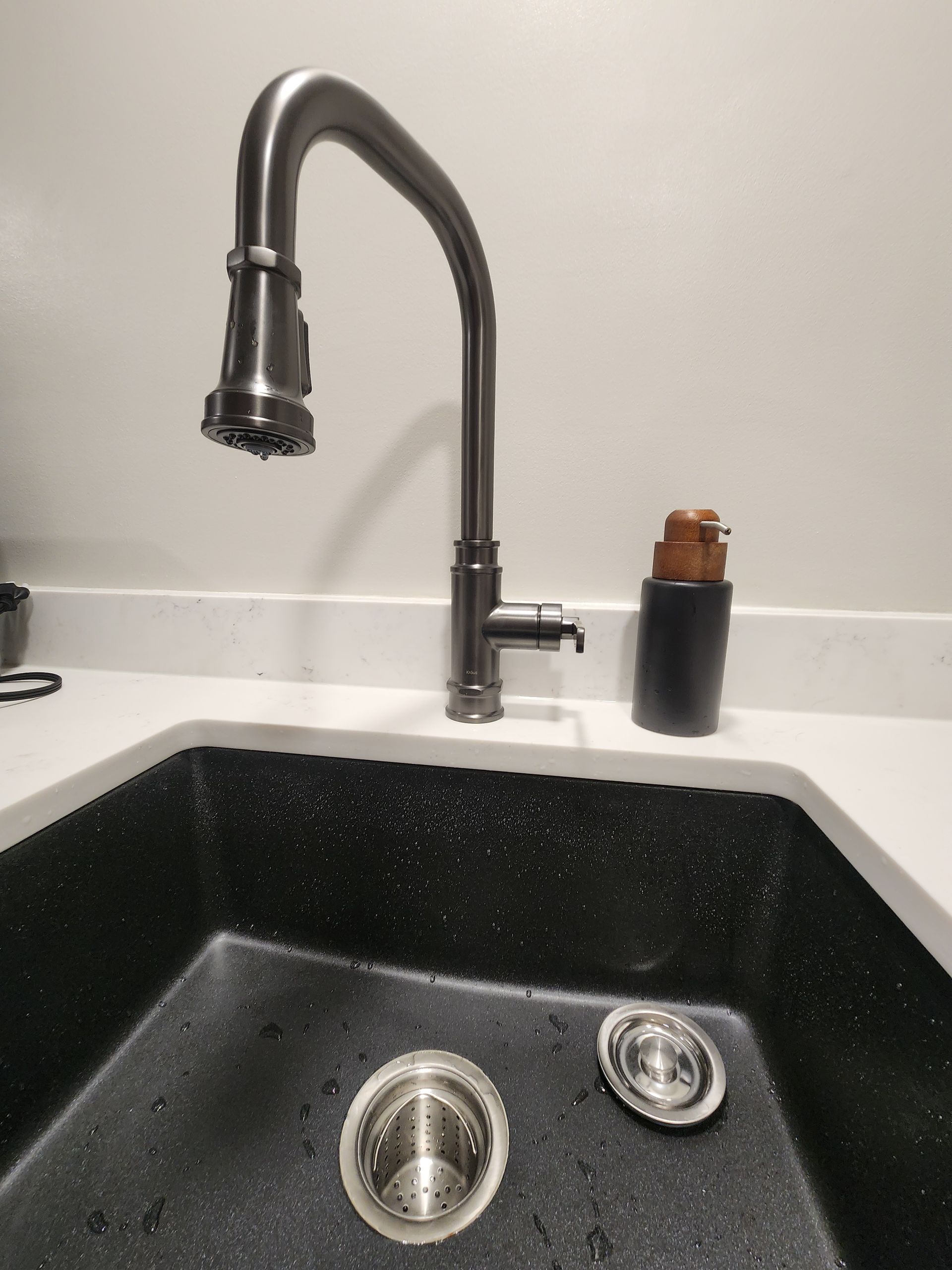 Kitchen sink with a tall, arched faucet, black sink basin, and soap dispenser.
