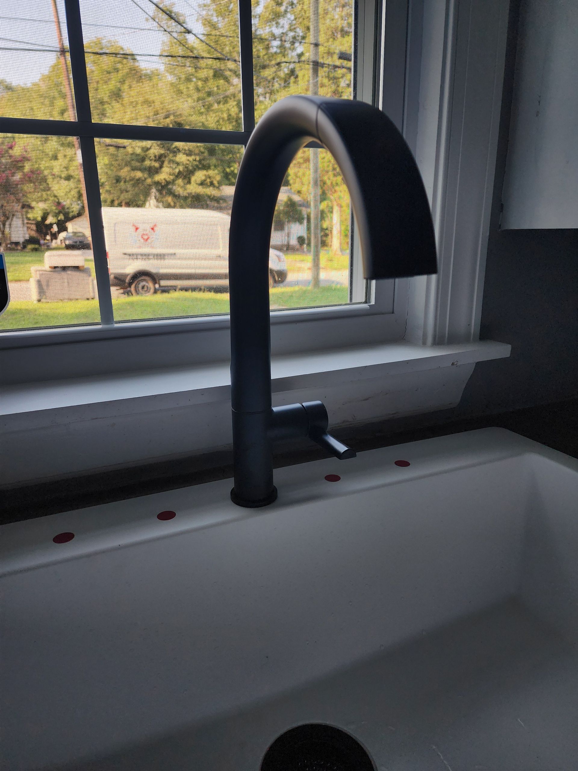 Black kitchen faucet over a white sink, set by a window.