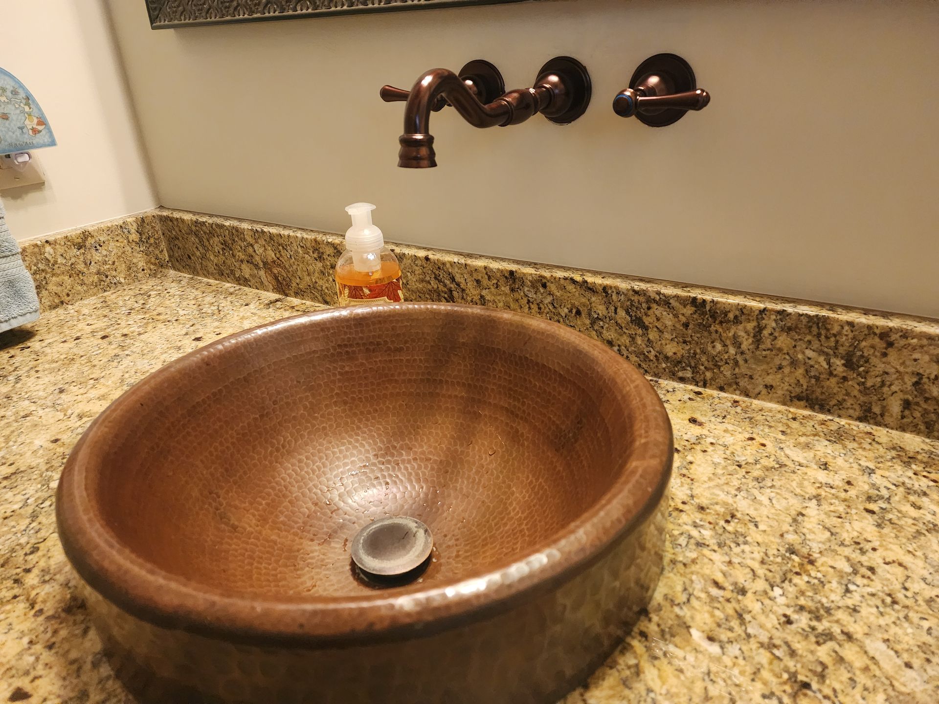 Copper bowl sink with wall-mounted faucet and granite countertop.