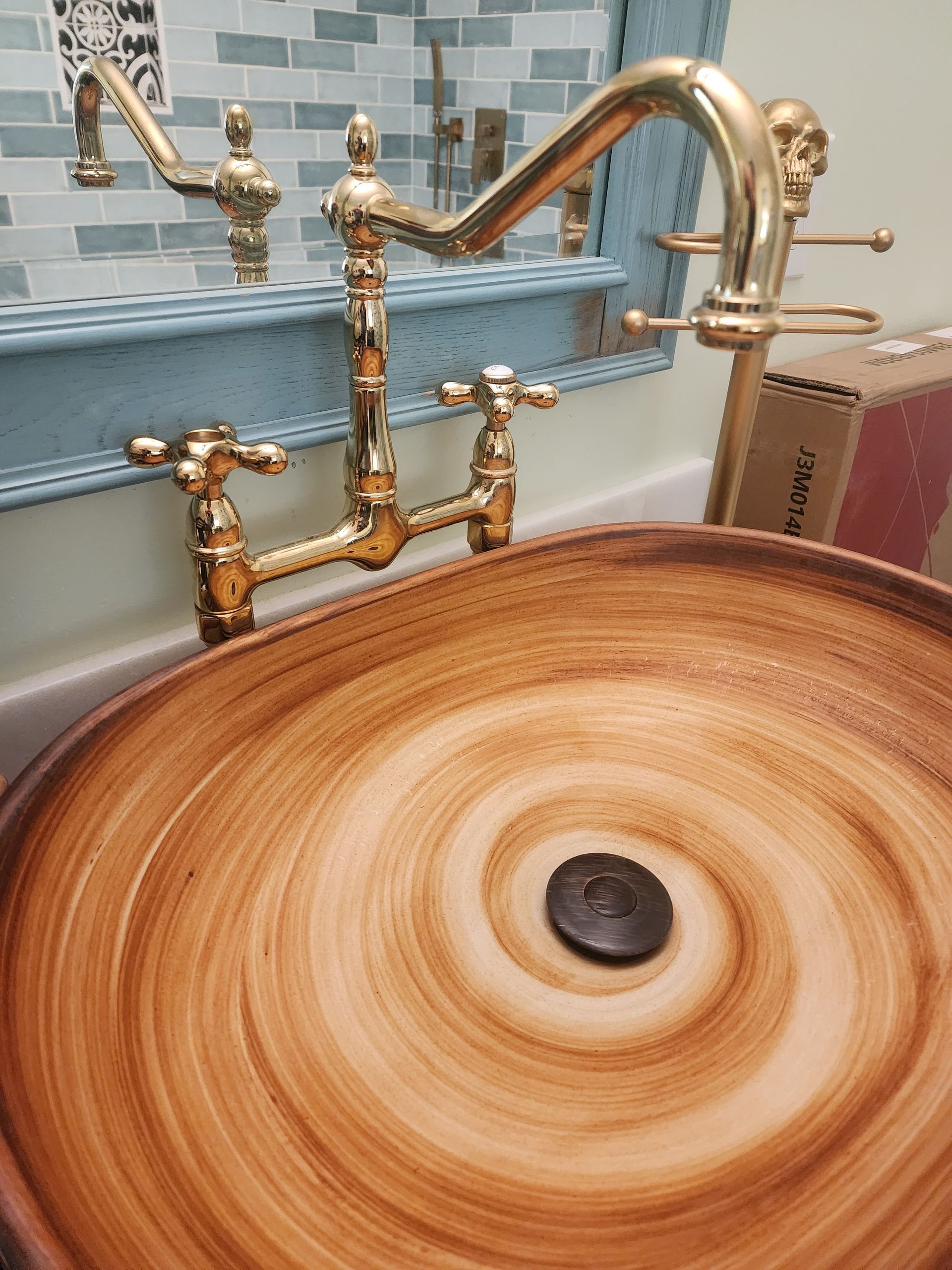 Gold faucet over a wood-grain bowl sink. Decorative blue shelf with gold towel racks.