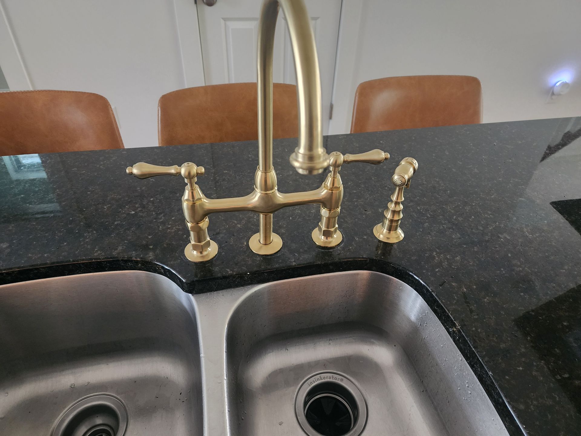 Gold kitchen faucet with sprayer over stainless steel double sink on black countertop.