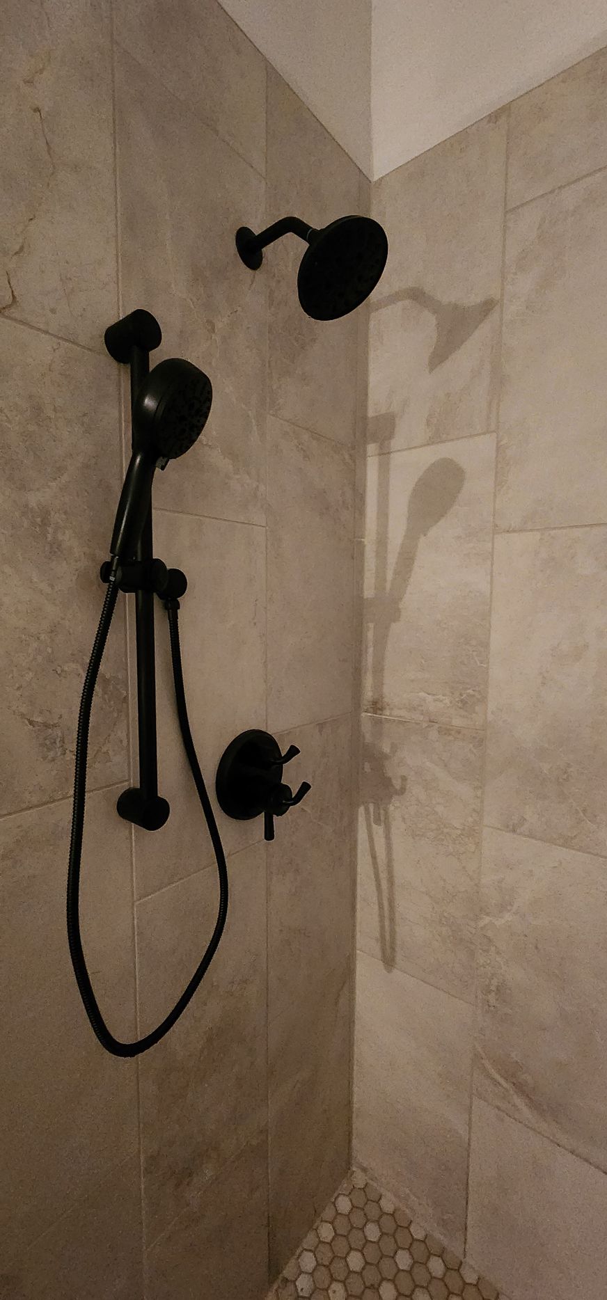 Black shower fixtures on beige tiled wall.