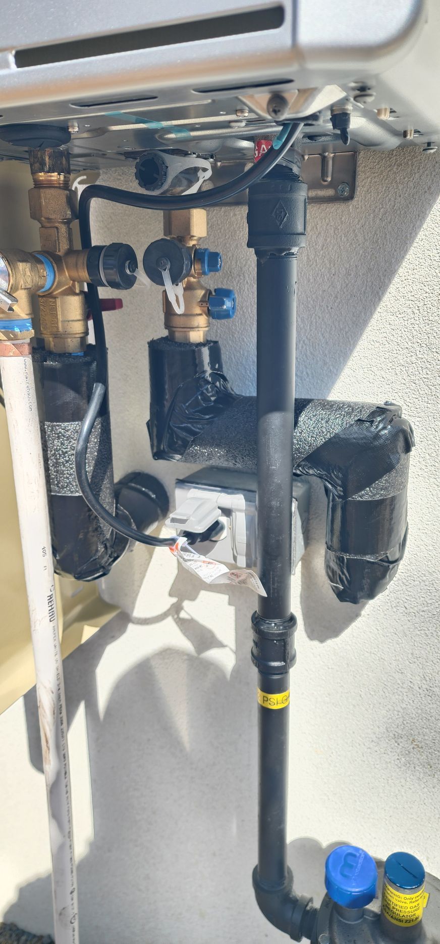Pipes and valves connected to a water heater. The metal unit is mounted on a wall.