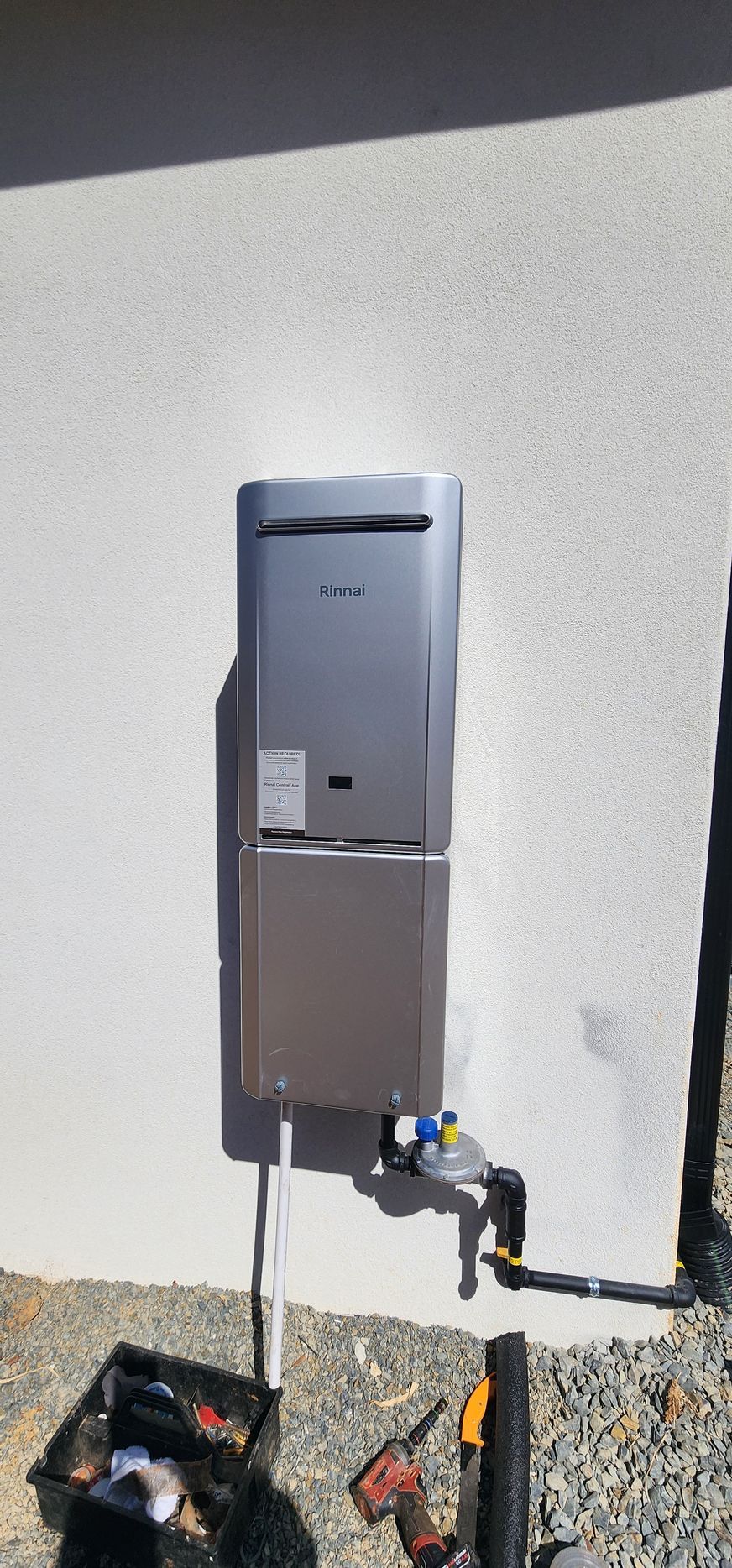Water heater mounted on a white wall, with plumbing and tools at the bottom.