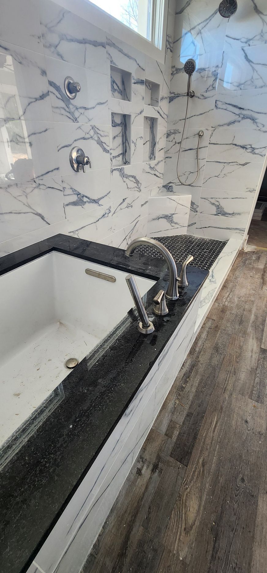 Bathroom with a marble tile shower and black countertop with a faucet. A white tub is visible.