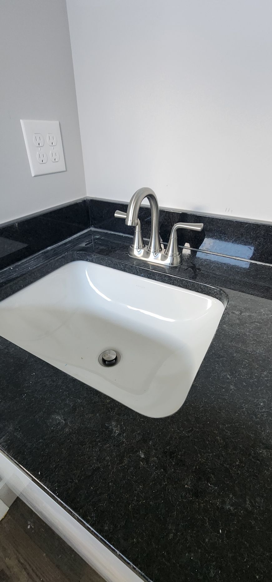 A bathroom sink with a black countertop and a faucet. The sink is white, and the wall is gray.