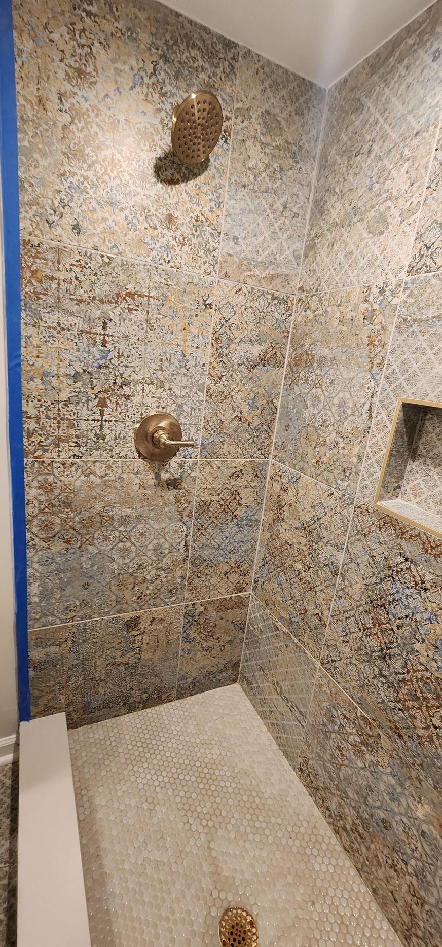 Shower with mosaic tile walls and floor, gold shower fixtures.