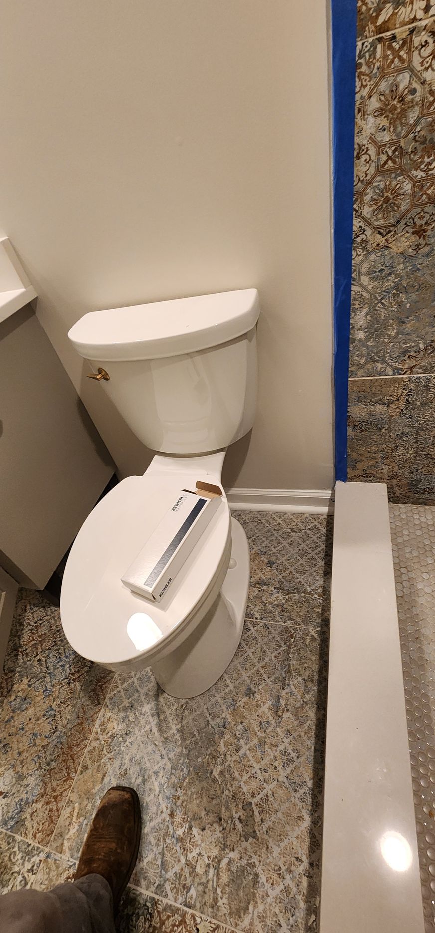 White toilet in a bathroom with patterned flooring and a blue taped wall.