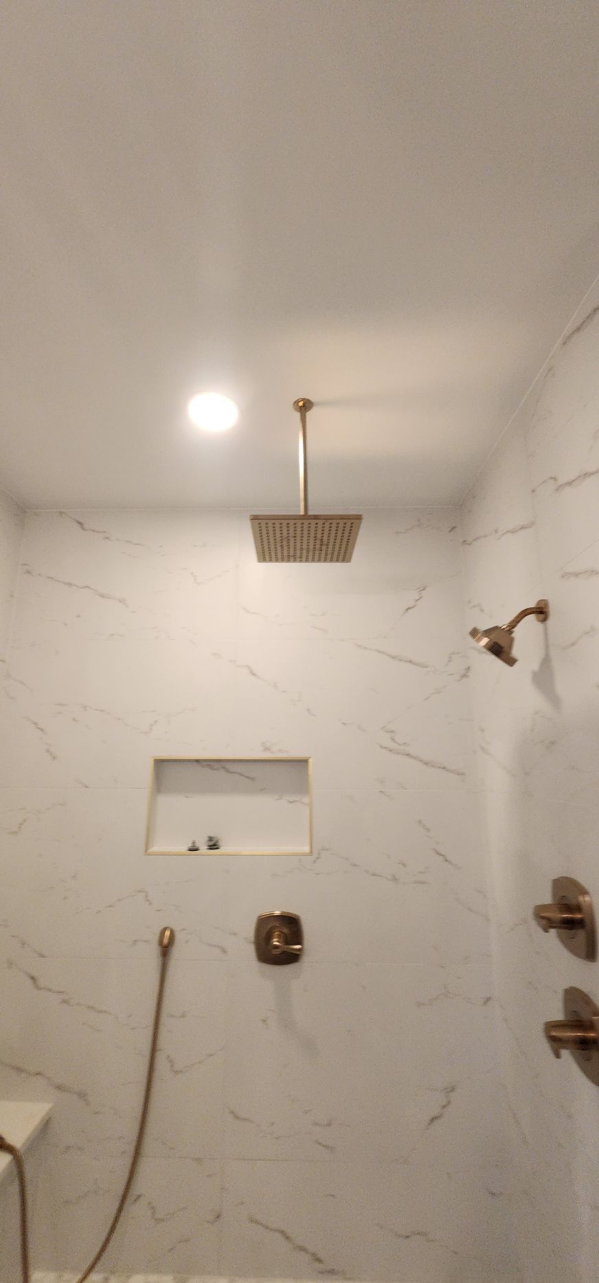 A modern marble shower with copper fixtures including a rain shower head, hand-held shower, and controls.
