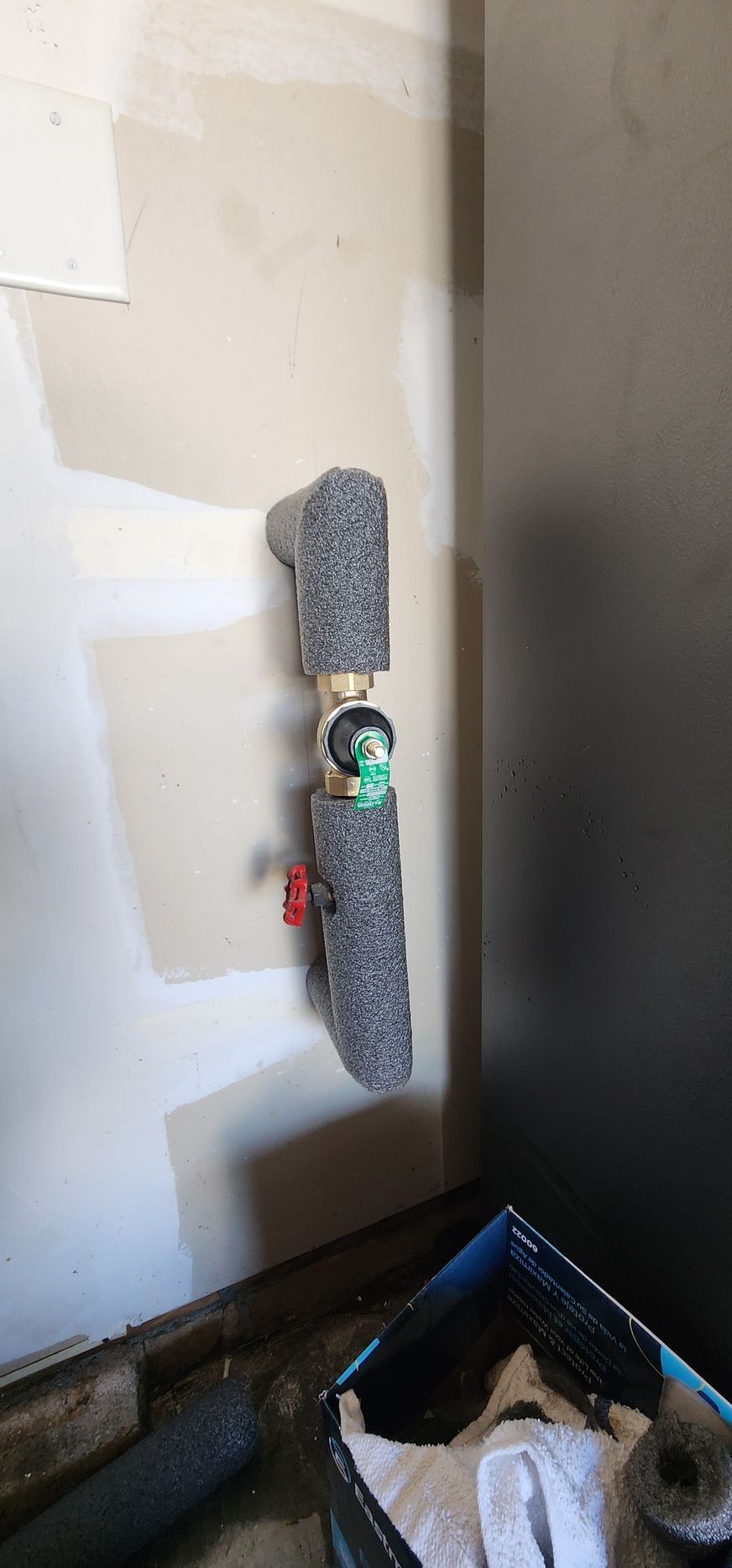 Pipes wrapped in grey insulation attached to a light-colored wall, red valve visible.