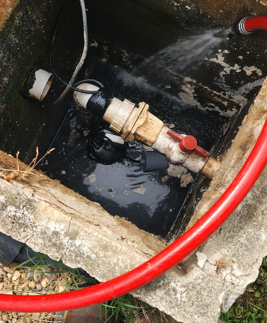 Water leaks from pipes inside a concrete box. A red hose is visible.