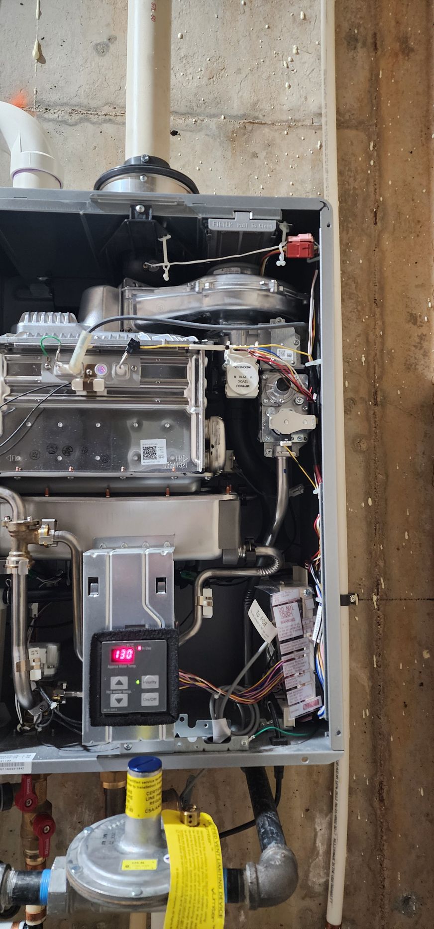 Opened gas boiler, showing internal components and control panel. Mounted on a concrete wall.