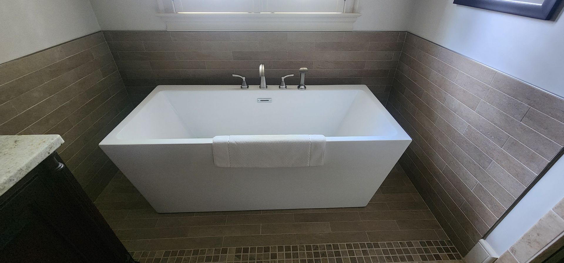 A white modern bathtub in a bathroom with brown tile walls and floors.
