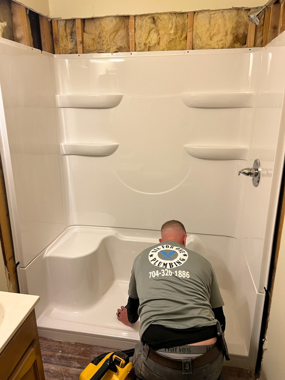 A person installing a white shower unit in a bathroom with exposed studs.
