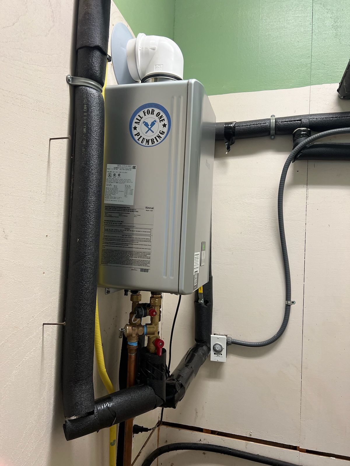 Silver tankless water heater on a wall with insulated pipes and copper fittings.