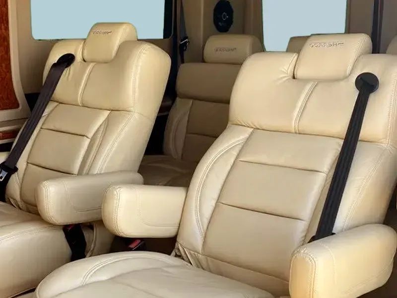 Two beige leather seats with black seat belts in a van