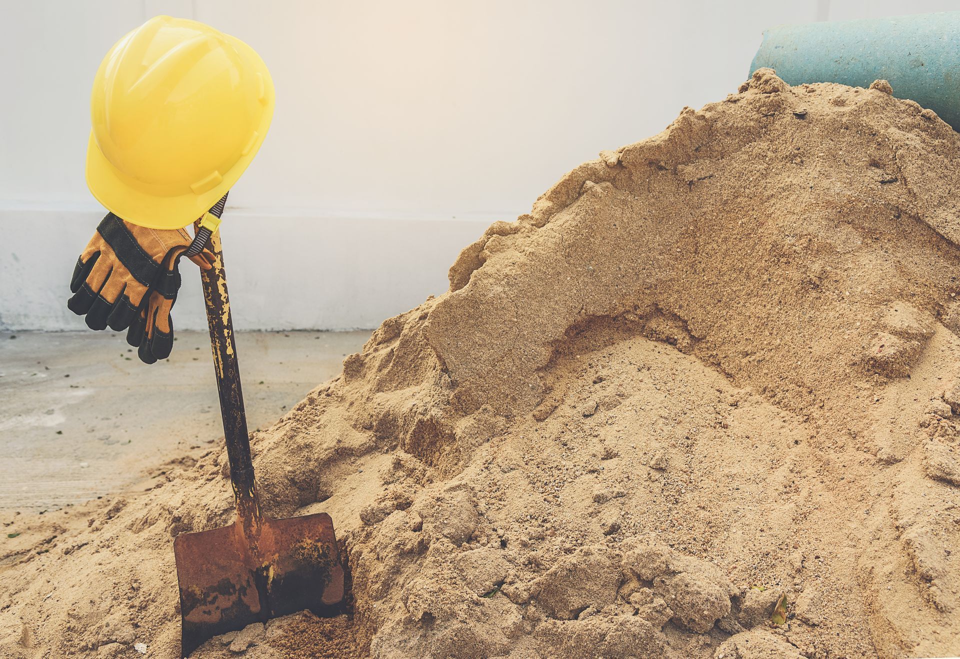 Casque jaune et gant de travail sur une pelle à côté d'un tas de sable.