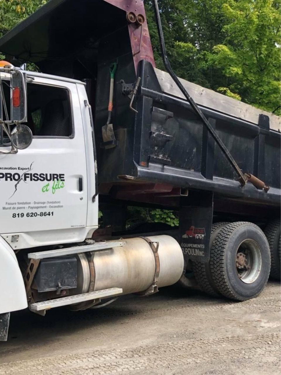 Camion-benne blanc à plateau noir stationné sur un sol meuble, outils fixés dessus, logo « Pro Fissure » visible.