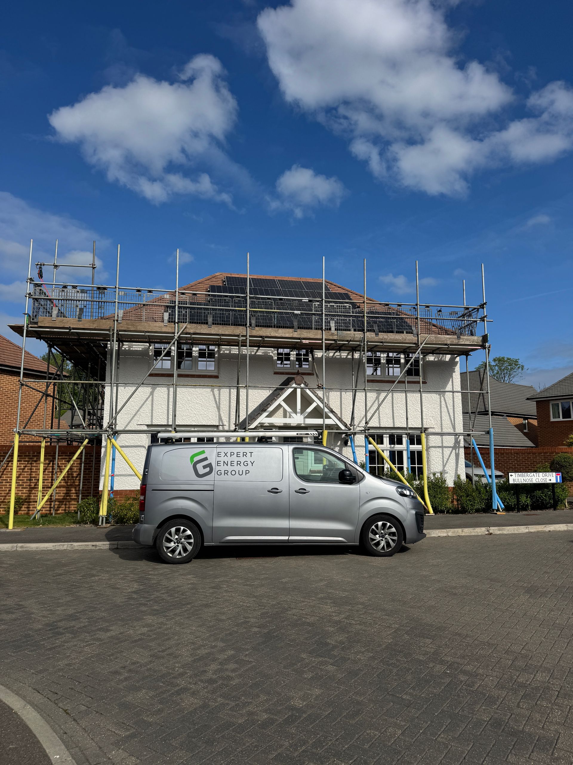 A white house under construction with scaffolding and a parked silver van under a blue sky.