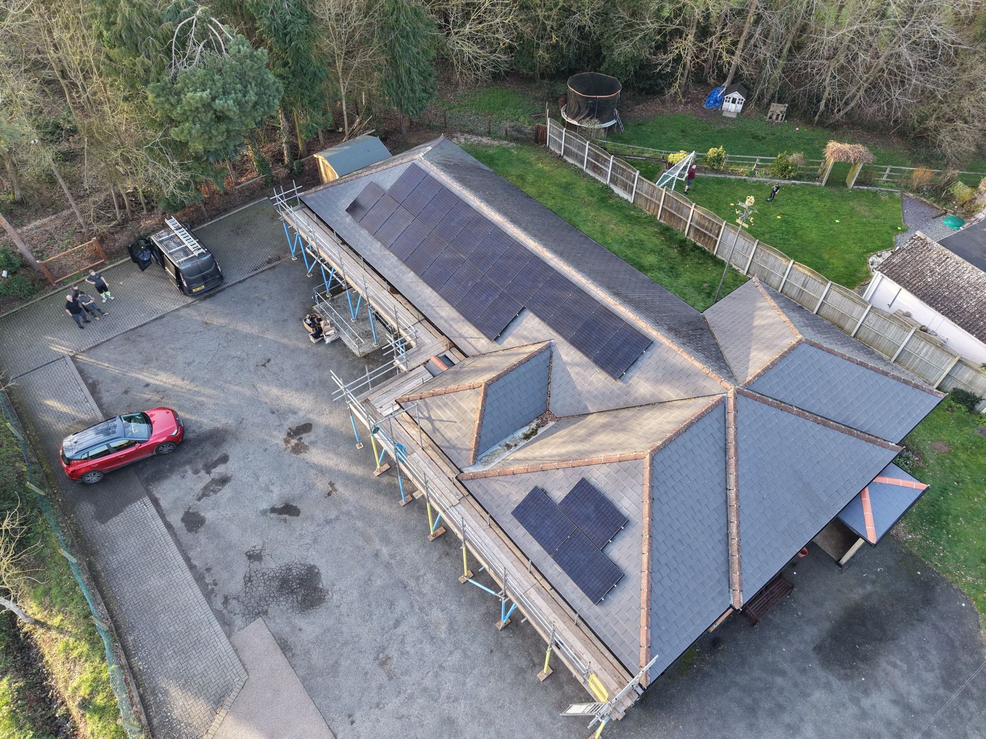 Building with a dark grey roof, a black side, and a brick side, with trees and a white house in the background. expert solar installation