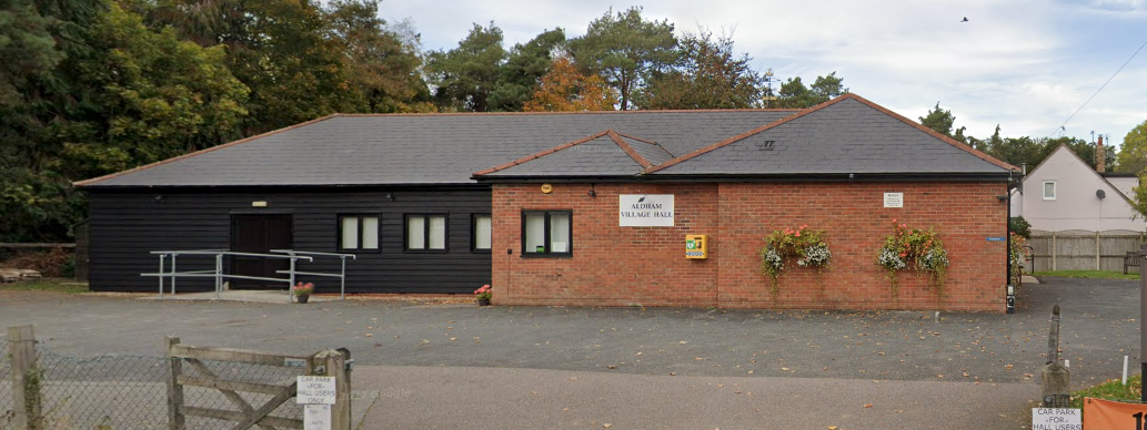 Building with a dark grey roof, a black side, and a brick side, with trees and a white house in the background. expert solar installation