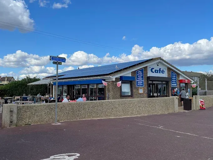 Cafe with solar panels on roof, patrons seated outside. Blue sky with clouds.