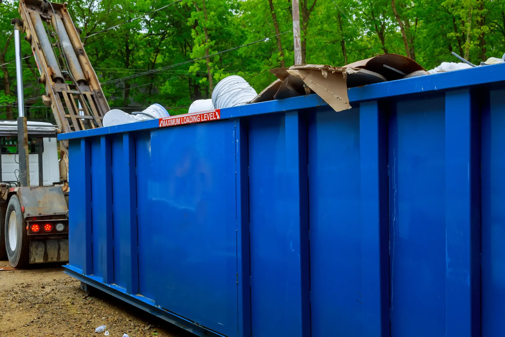 Blue dumpster filled with debris in an outdoor setting.