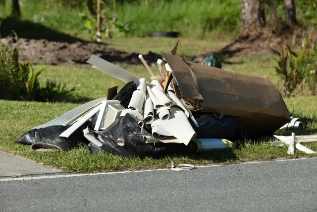 Pile of trash and debris on a grassy verge next to a paved road.