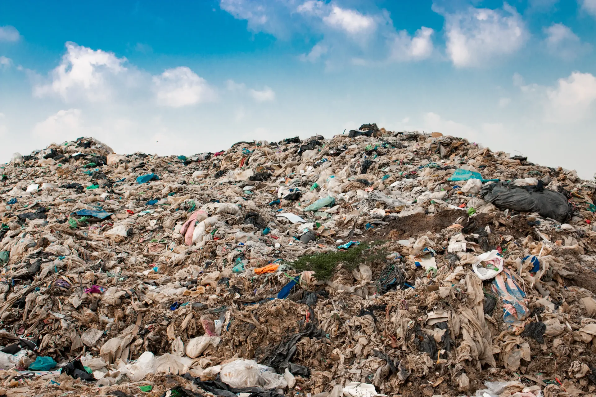 A massive, sprawling heap of varied trash and debris piled against a bright blue, cloudy sky.