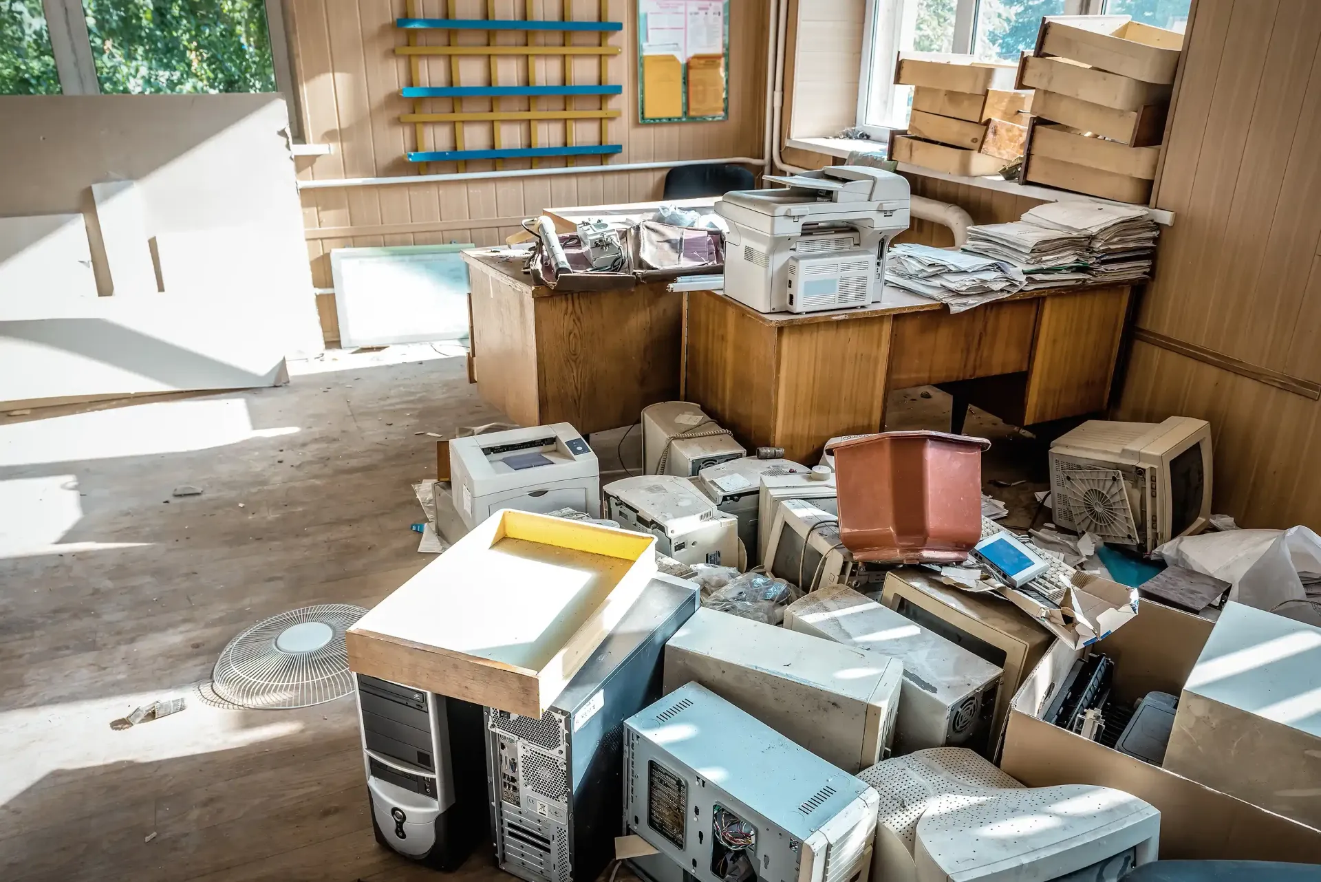 A cluttered office filled with old computers, printers, and stacks of paper.
