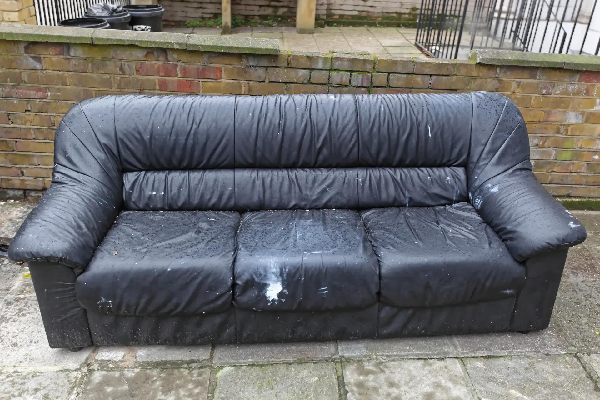 Black leather sofa on a brick patio, possibly outdoors.