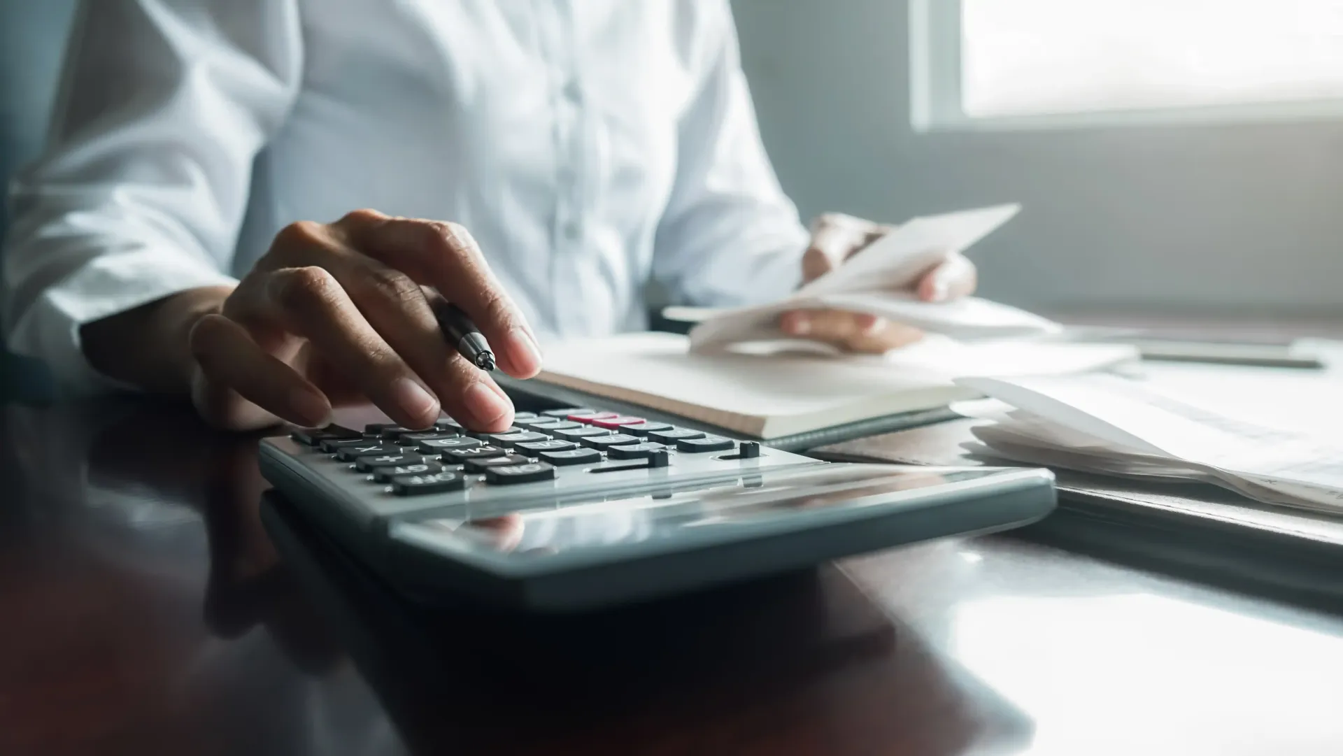A person in a white shirt sits at a desk, using a calculator and estimating a quote.