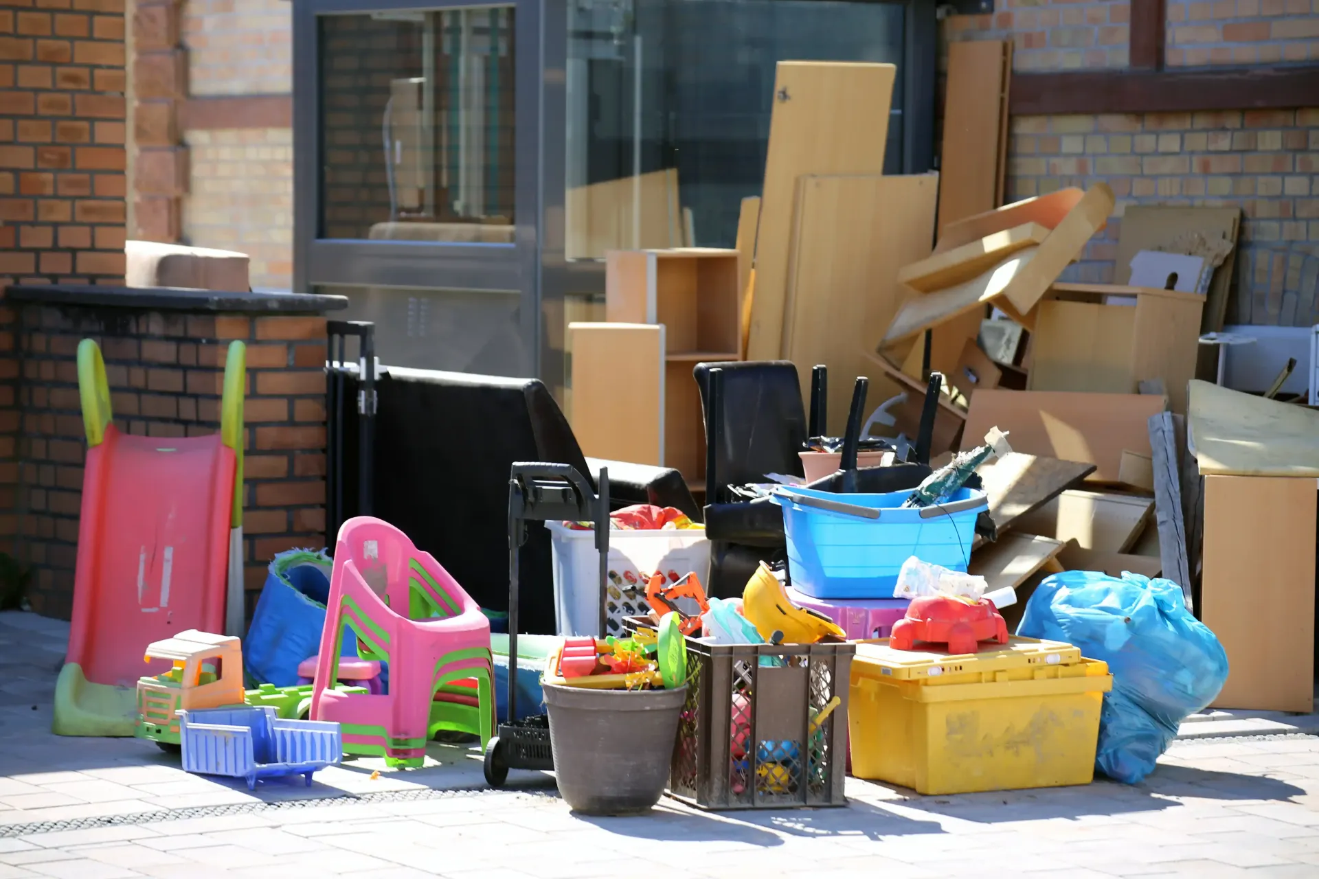 Pile of assorted junk, including cardboard boxes, plastic toys, and containers, next to a building.