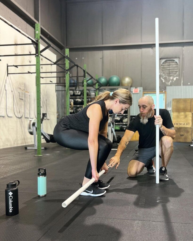 A man is helping a woman do a squat in a gym.