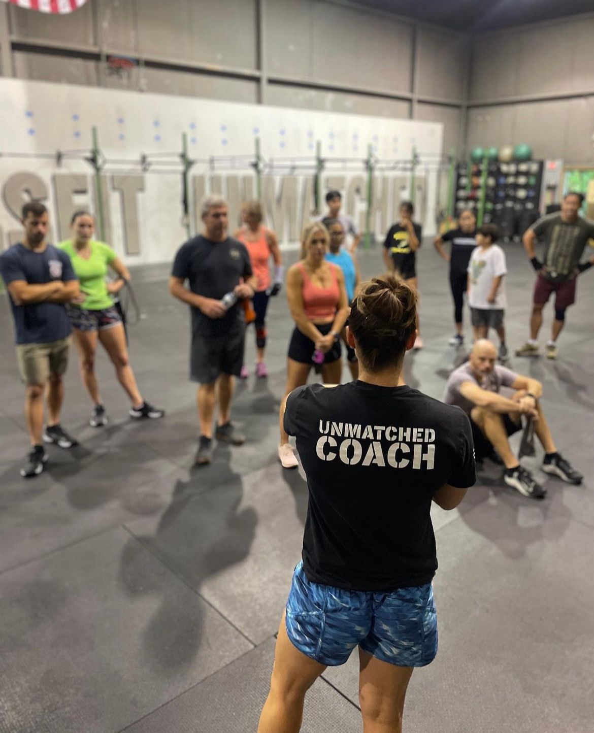 A woman wearing an unmatched coach shirt stands in front of a group of people