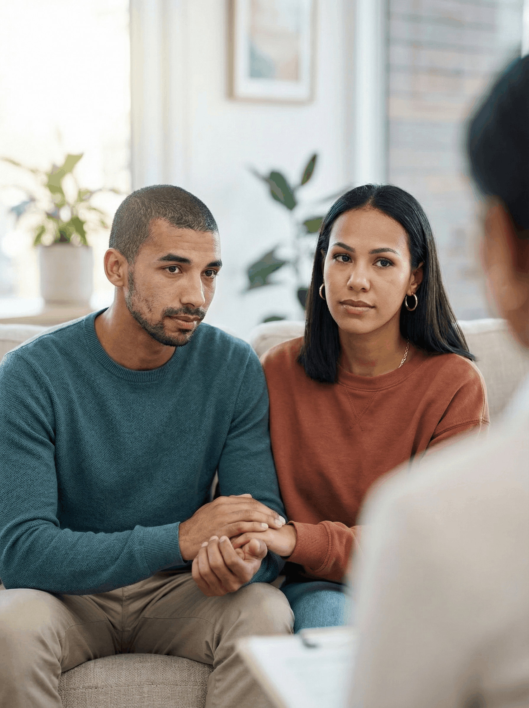 Man and woman sit on a gray sofa, man's arm around her. Both appear relaxed in a waiting area.