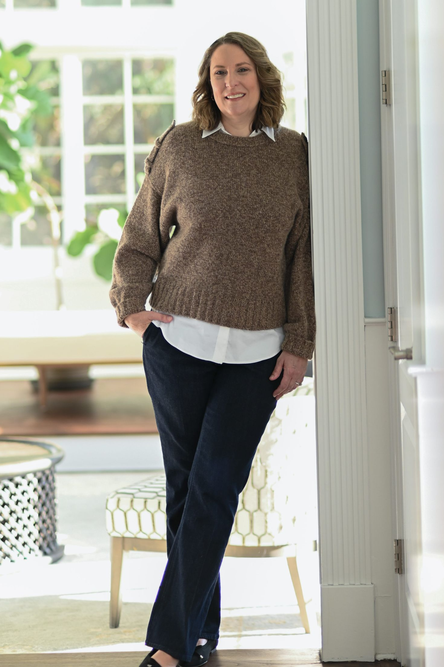 Woman smiling, wearing a burgundy leather jacket and cream-colored blouse, standing in front of a stone wall.