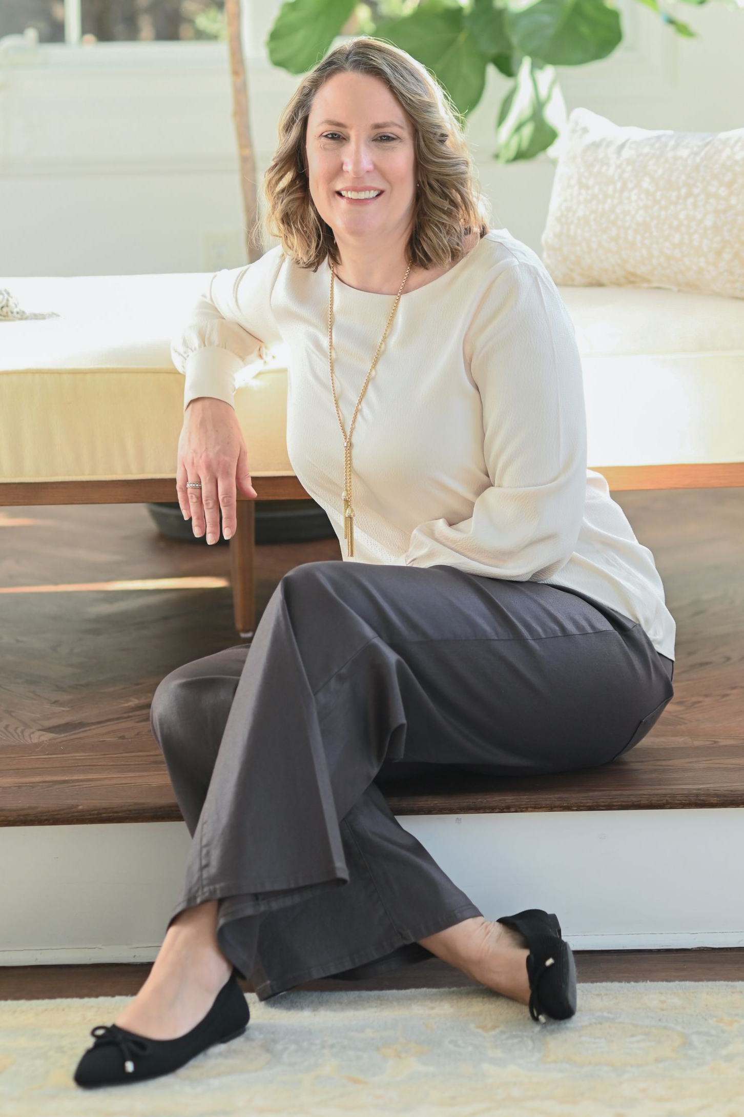 Woman smiling in front of a stone wall, wearing a maroon leather jacket and cream blouse.